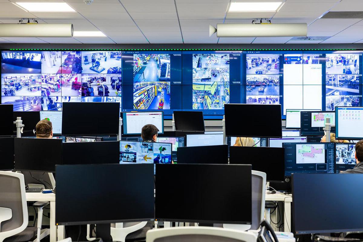 Various people working at desks with a wall of computer screens in front of them, showing a range of CCTV imagery